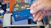 Hand holding a blue Visa card in front of a POS device
