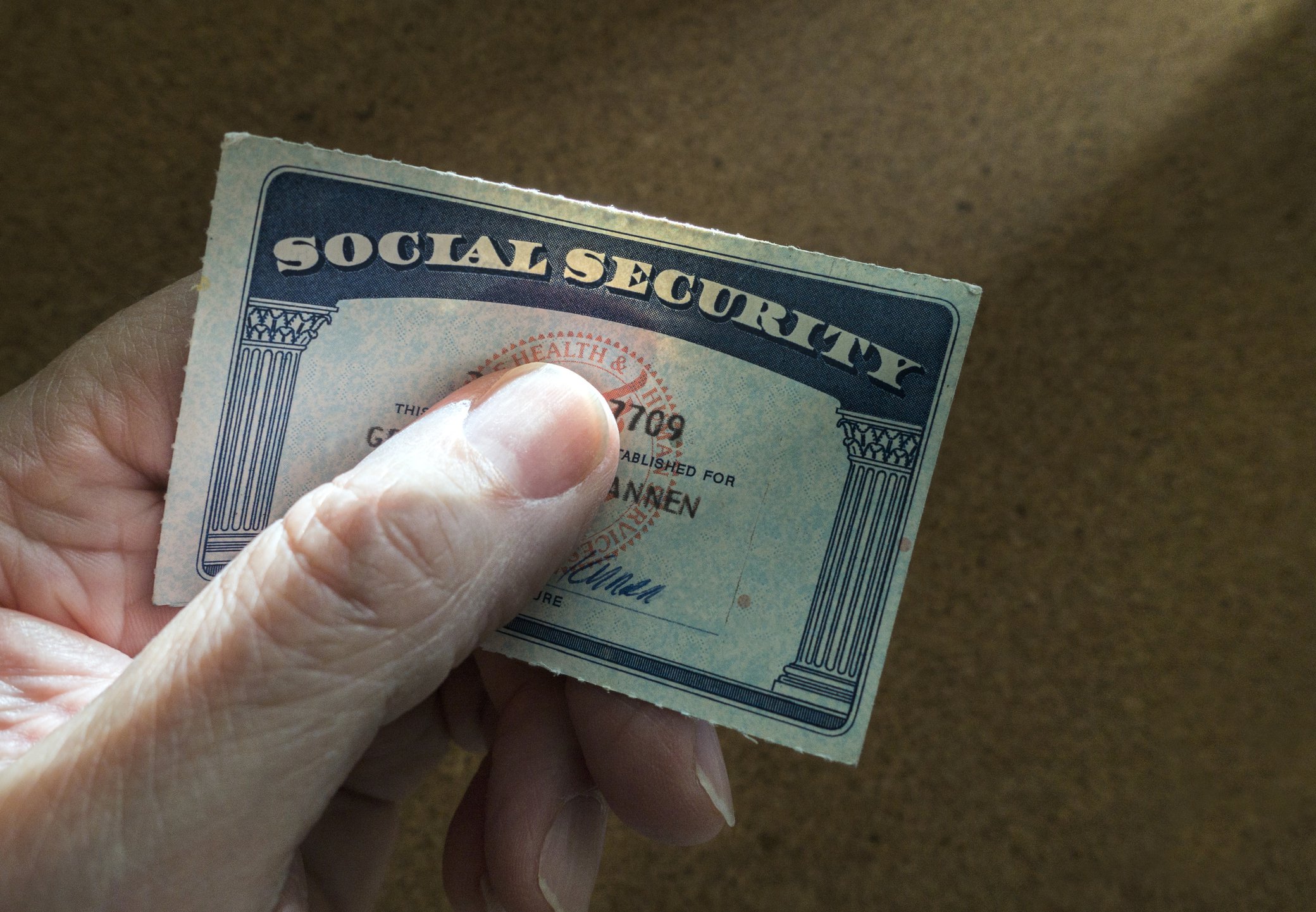 A person tightly grasping a social security card under their thumb.