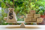 Burlap sack of money balanced on a seesaw versus stocks, bonds, and more
