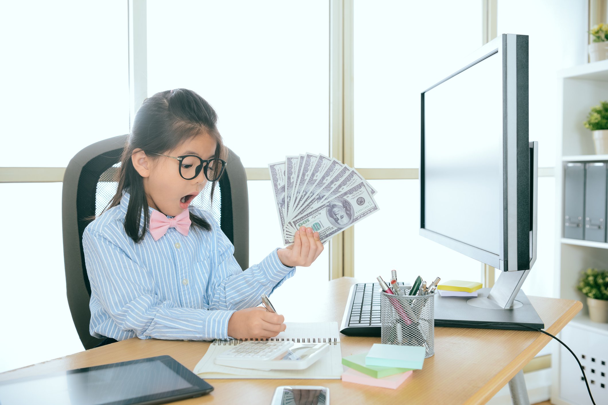 Child in glasses at desk with cash and surprised look on her face