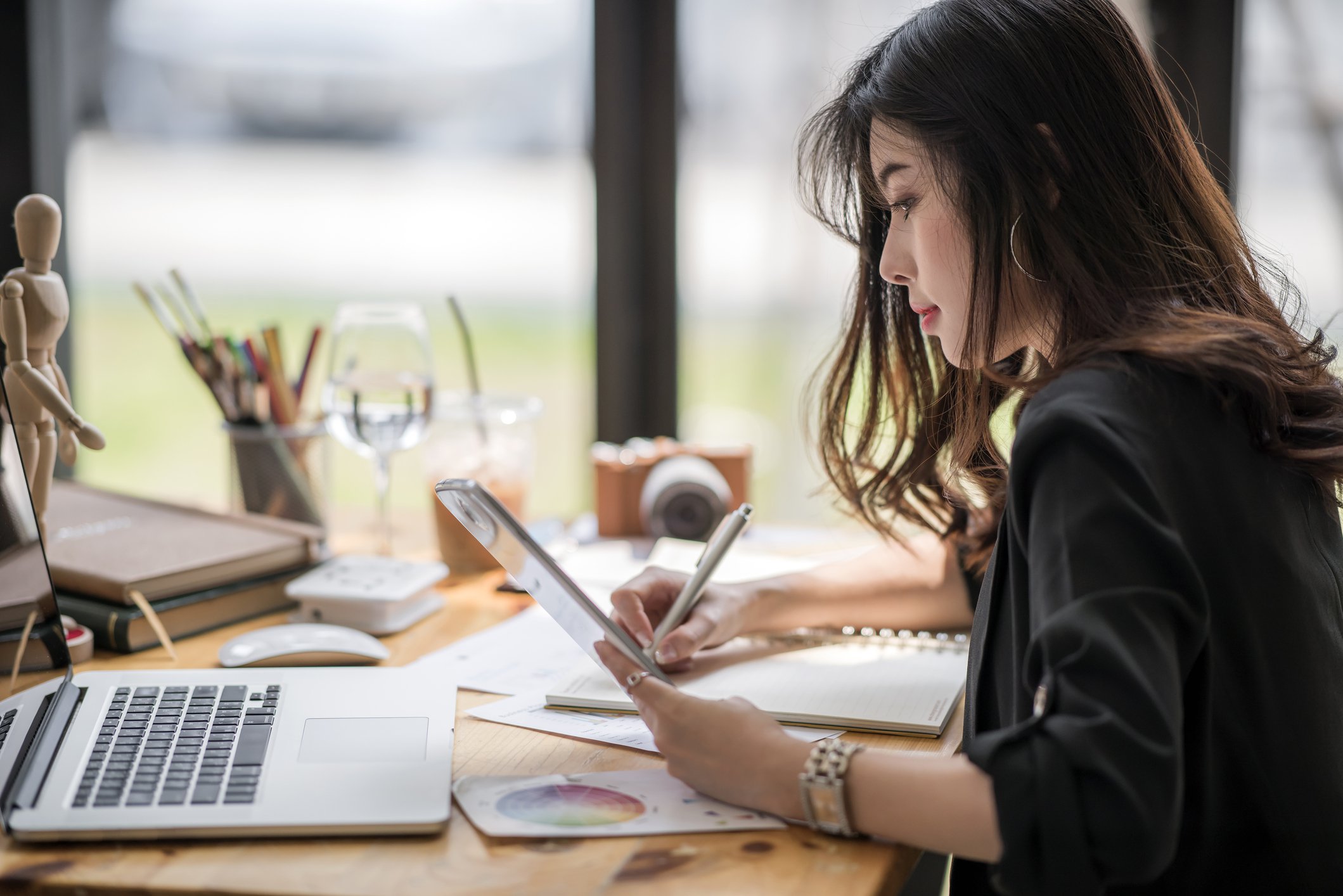 Female designer looking at tablet and writing note