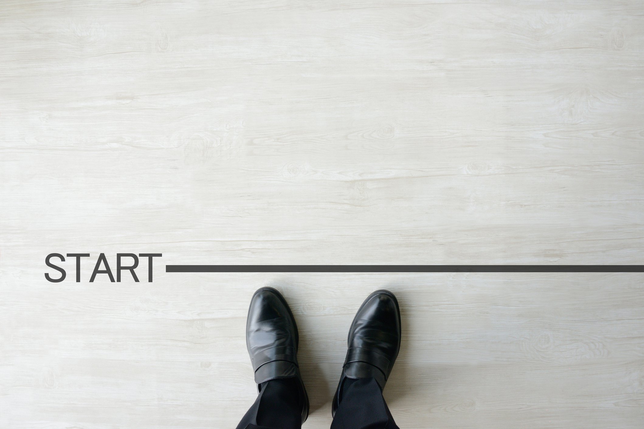 Two feet in business shoes standing behind a line marked START.