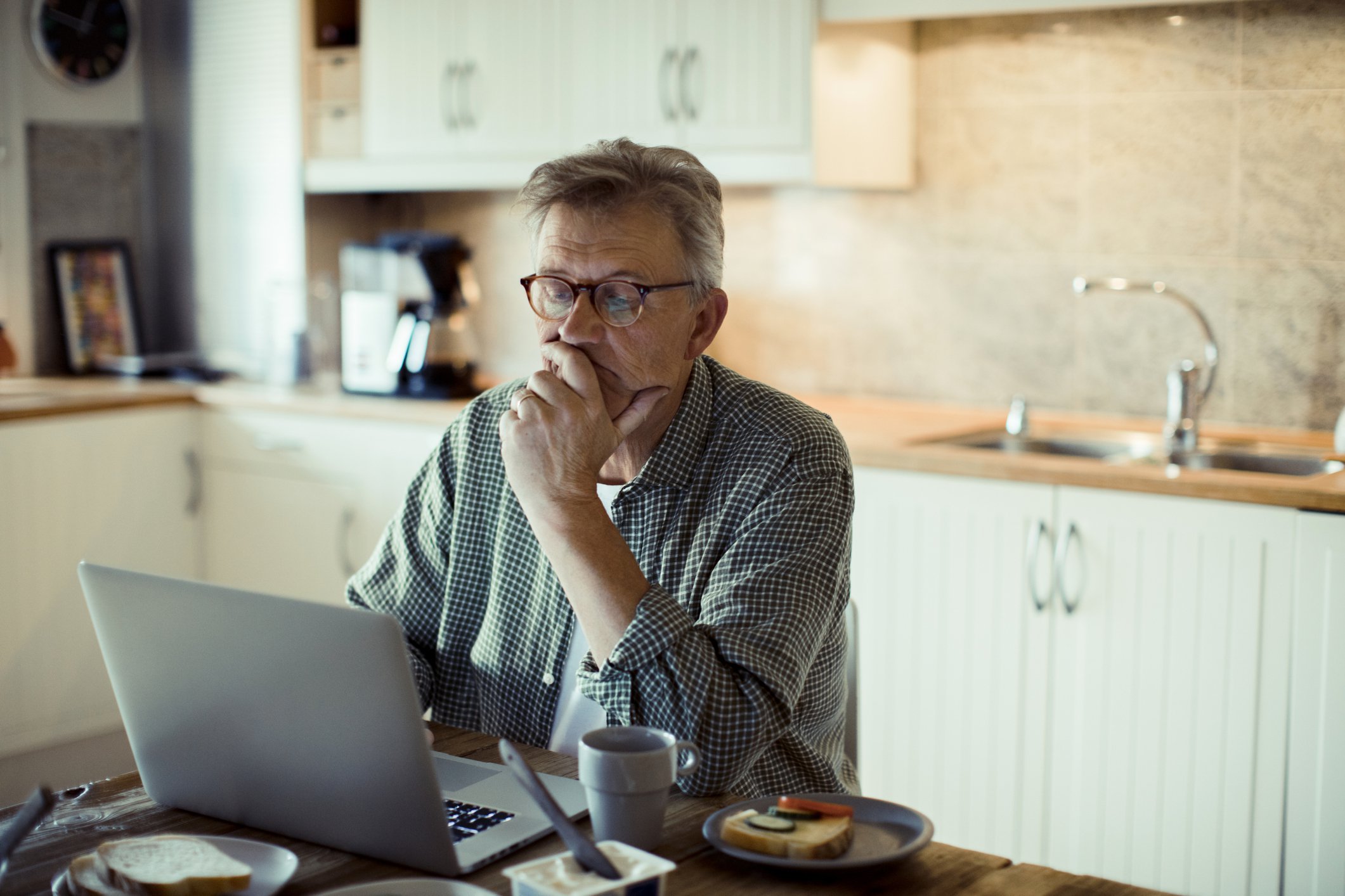 Older man sitting in the kitchen and looking at a laptop