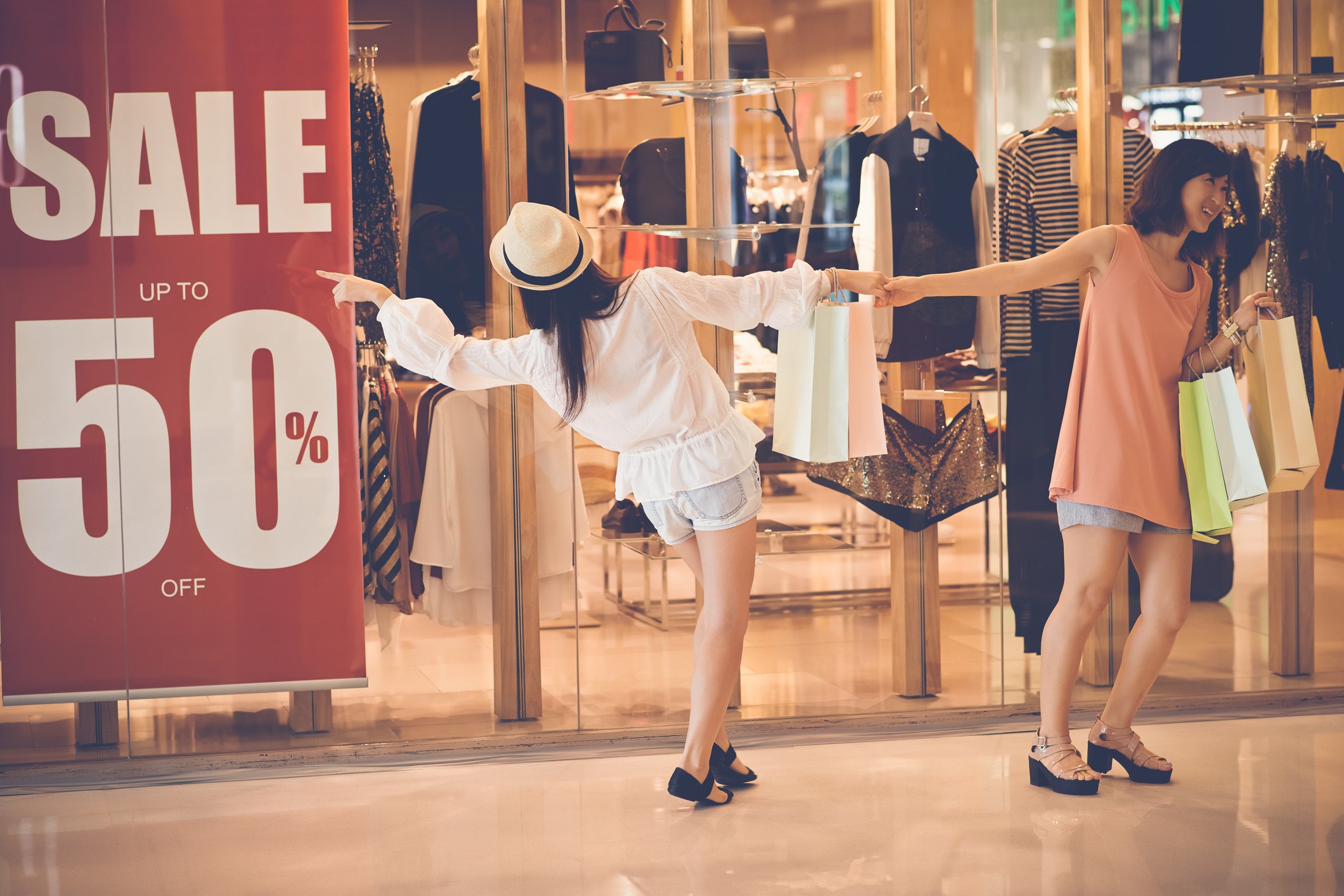 One woman pulling another away from a 50% off sale sign.