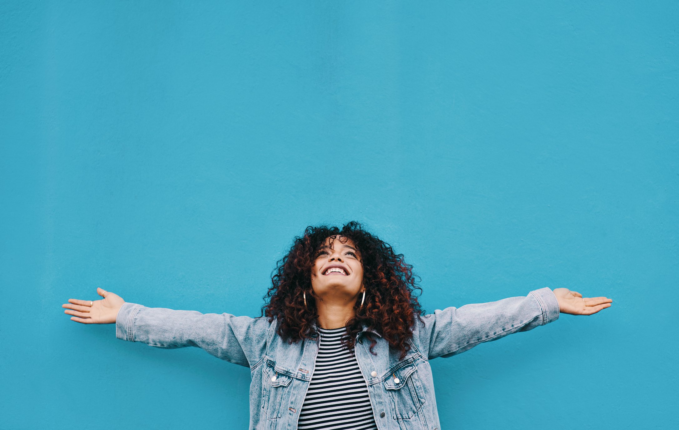 Person looking up with smile and arms spread outward against blue background.