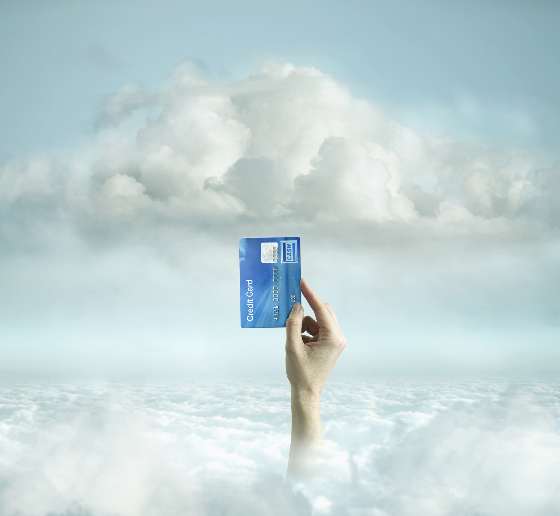 Hand holding credit card up against background of white clouds and blue sky