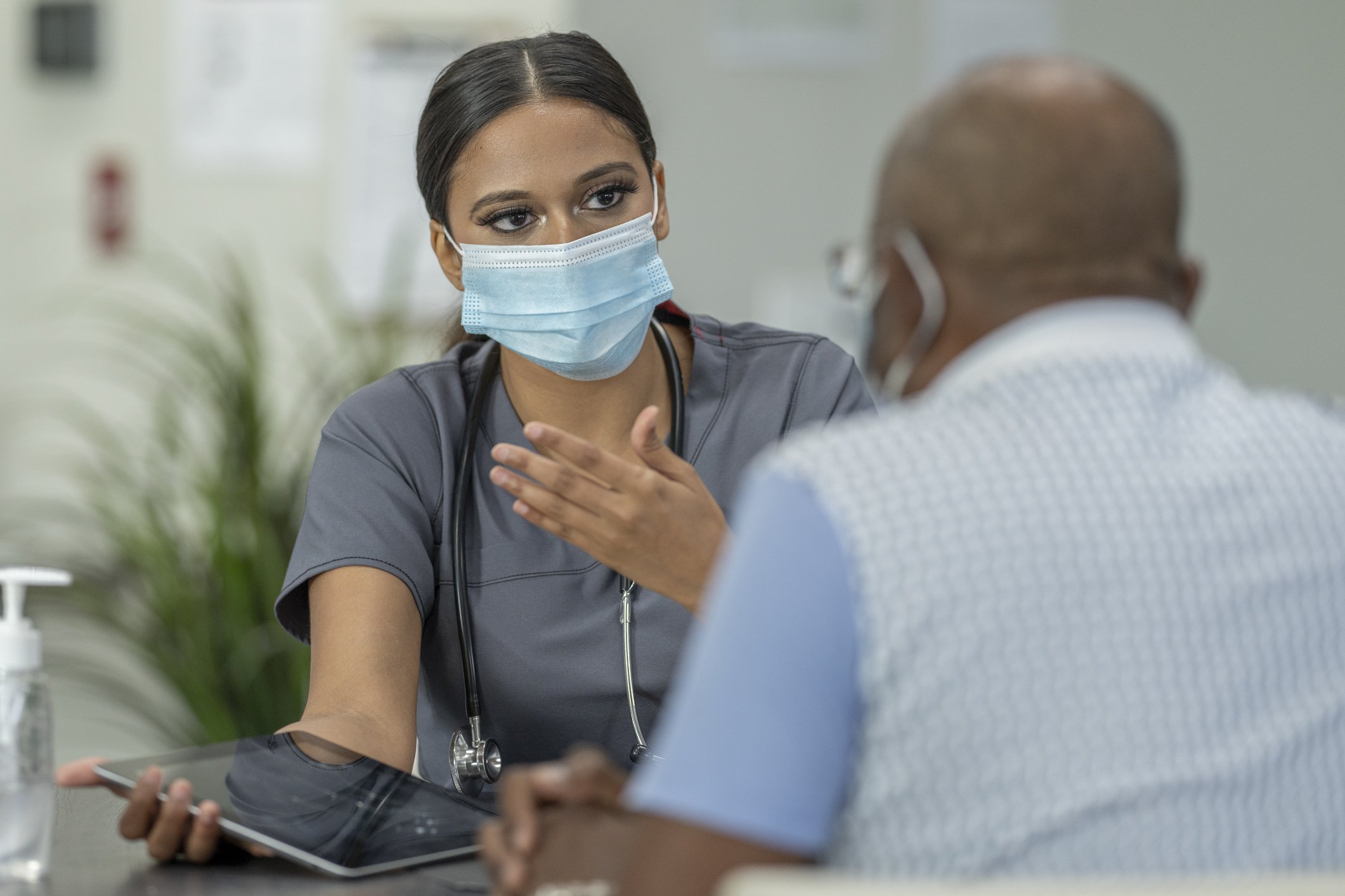 Nurse in mask speaking with patient and holding tablet