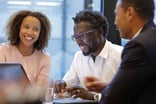 Three smiling people looking at device screen in office.