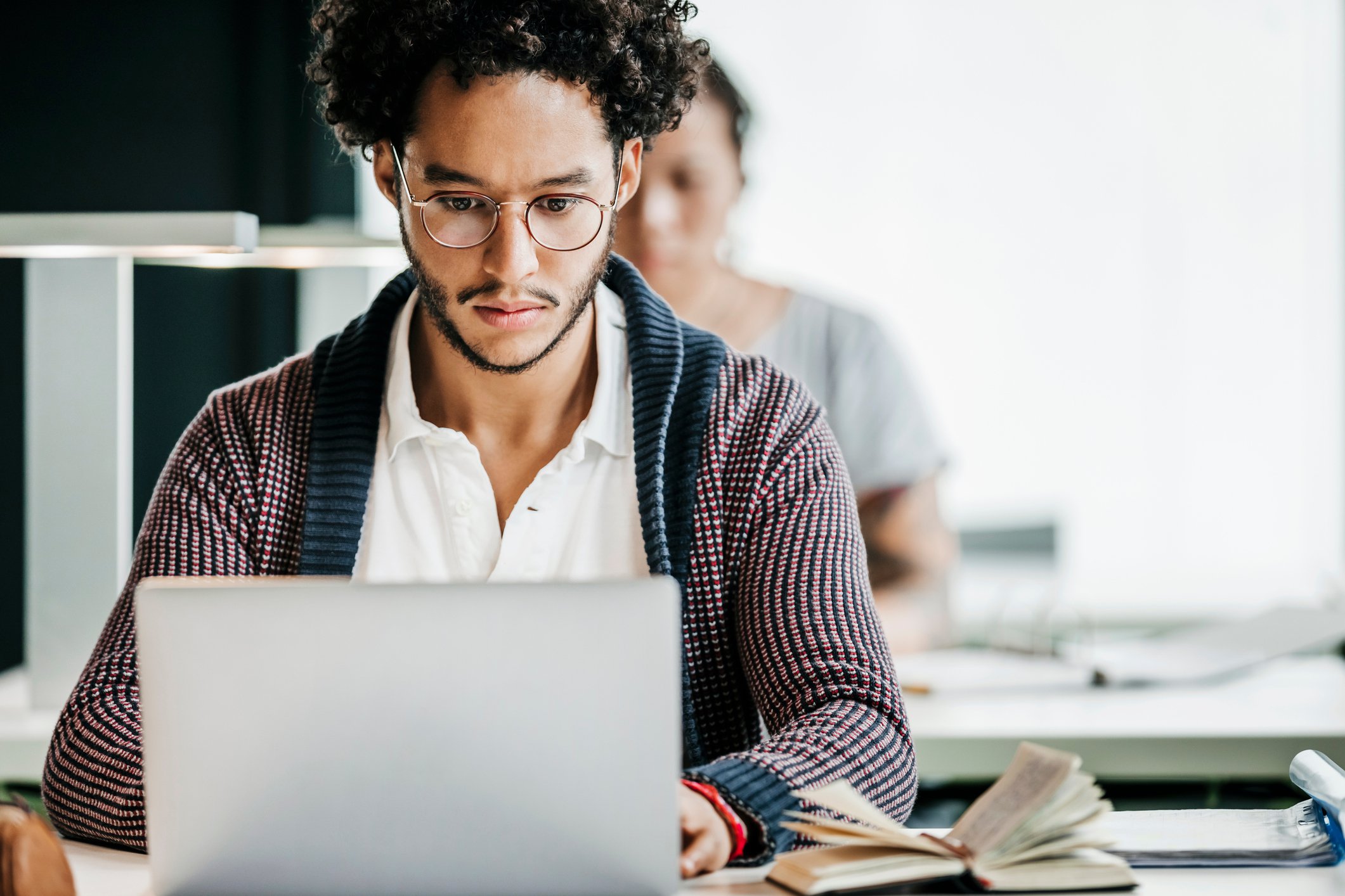 Young man wearing glasses and cardigan is looking at laptop screen.
