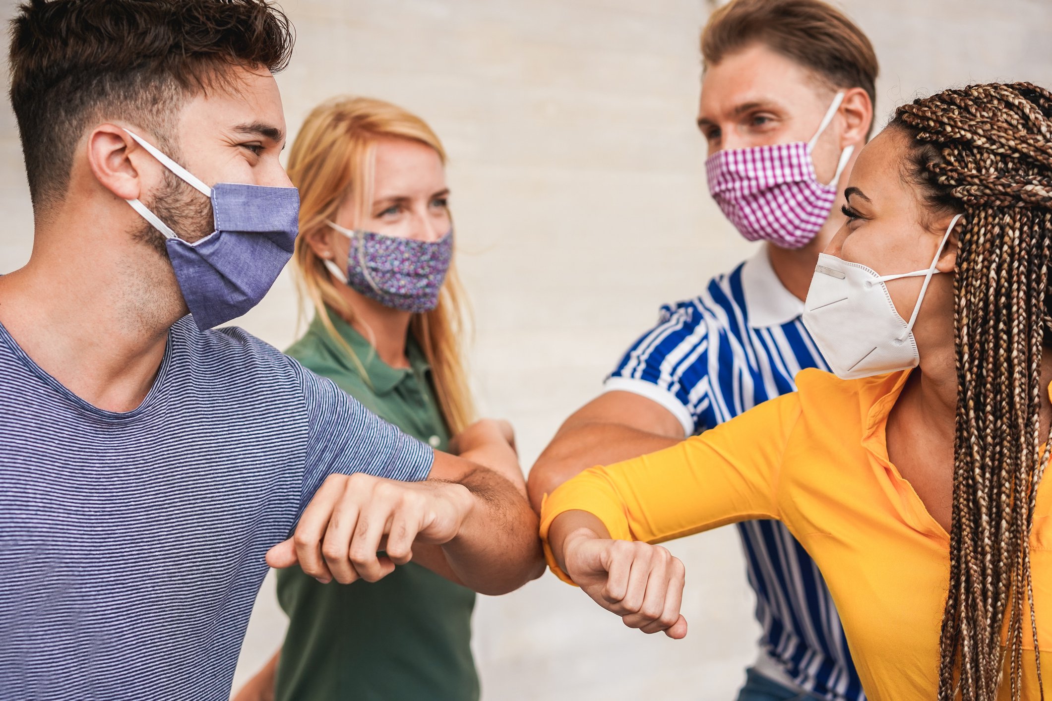 Group of young millennials wearing face masks and elbow bumping