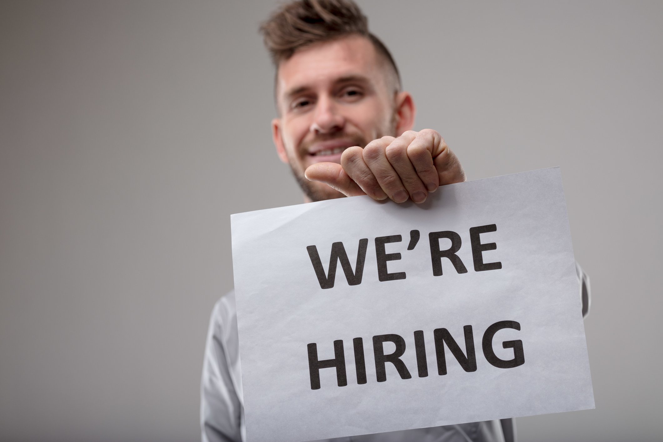 Smiling man holding We're Hiring sign.