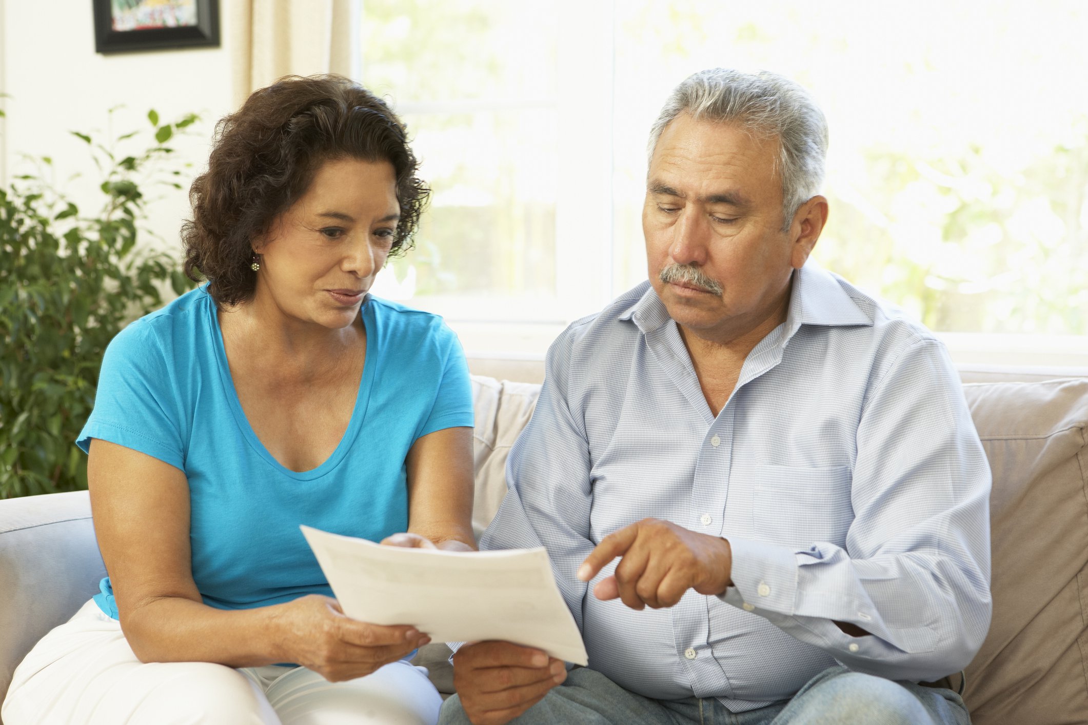 Senior couple sitting on couch and pointing at document.