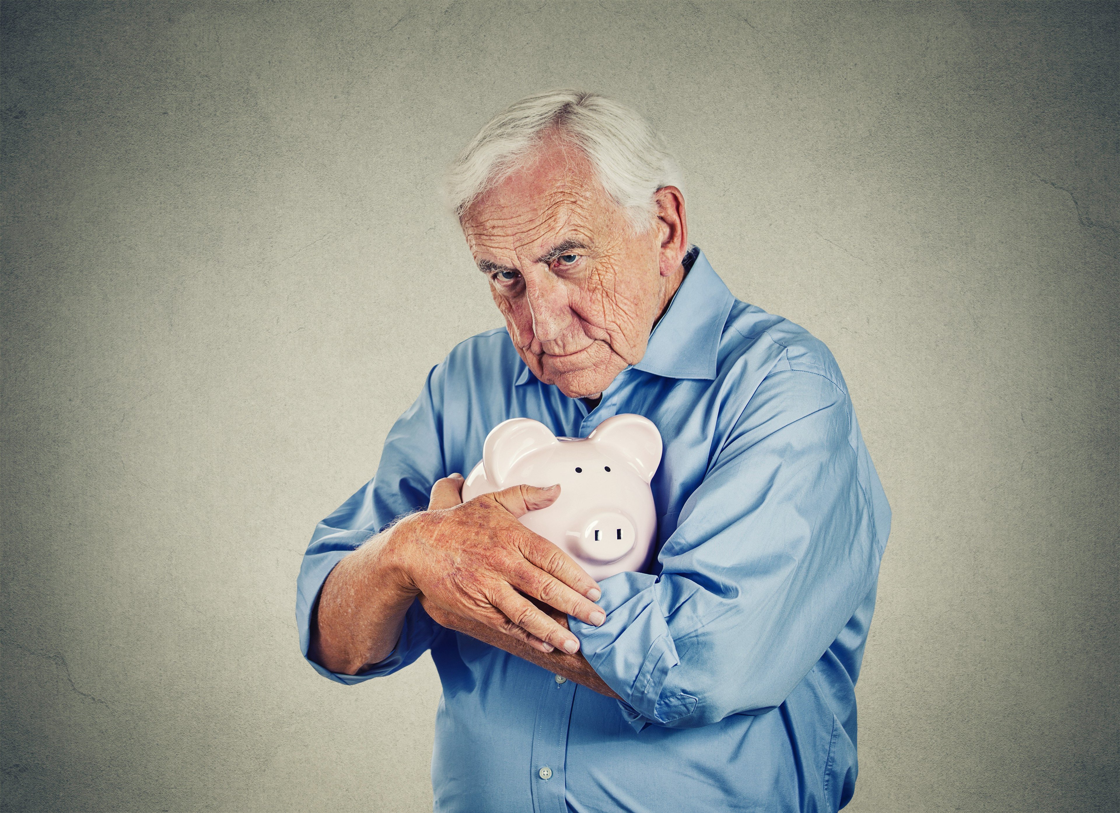 A senior man clutches a piggy bank to his chest.