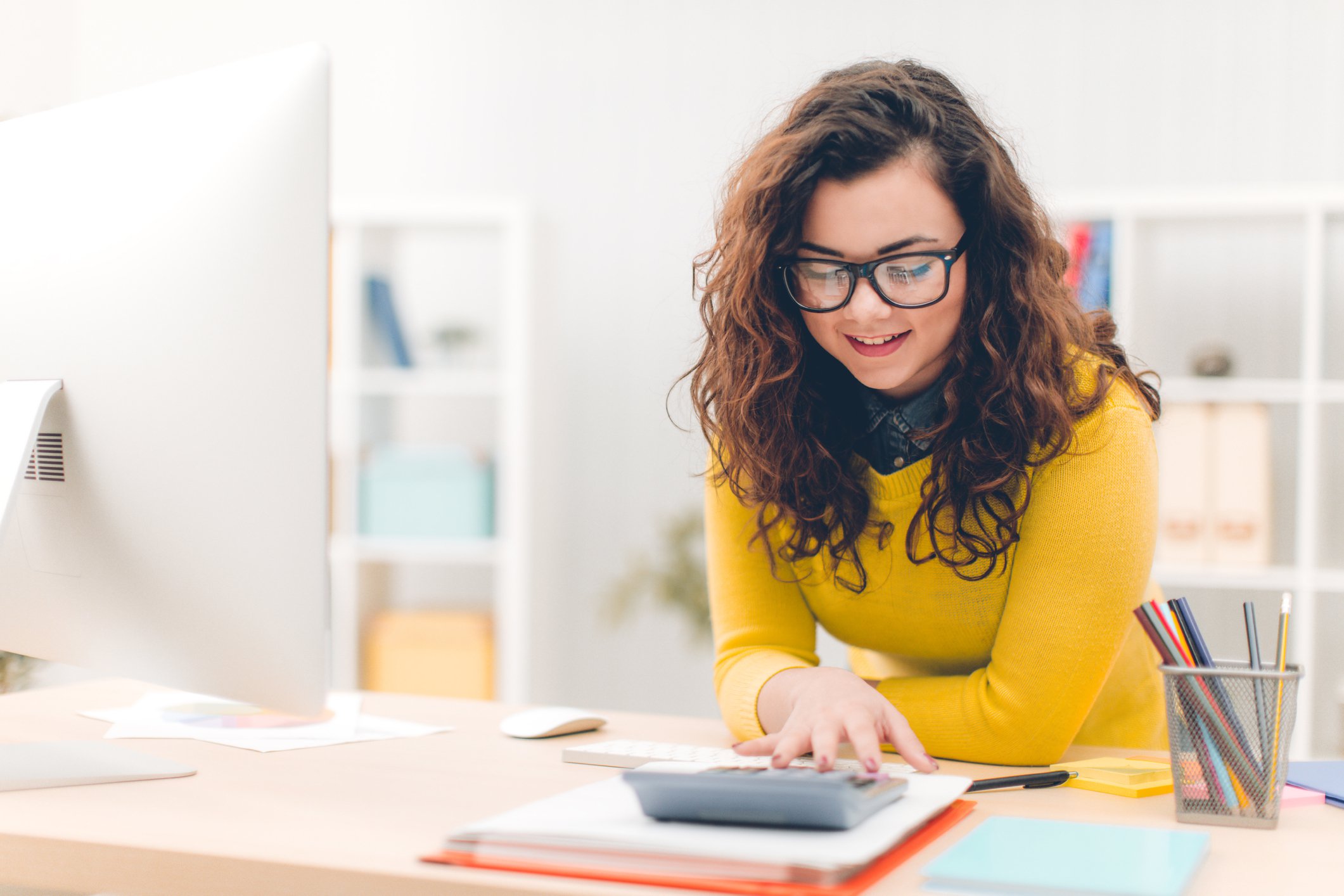 Young woman smiling using calculator and reviewing paperwork.