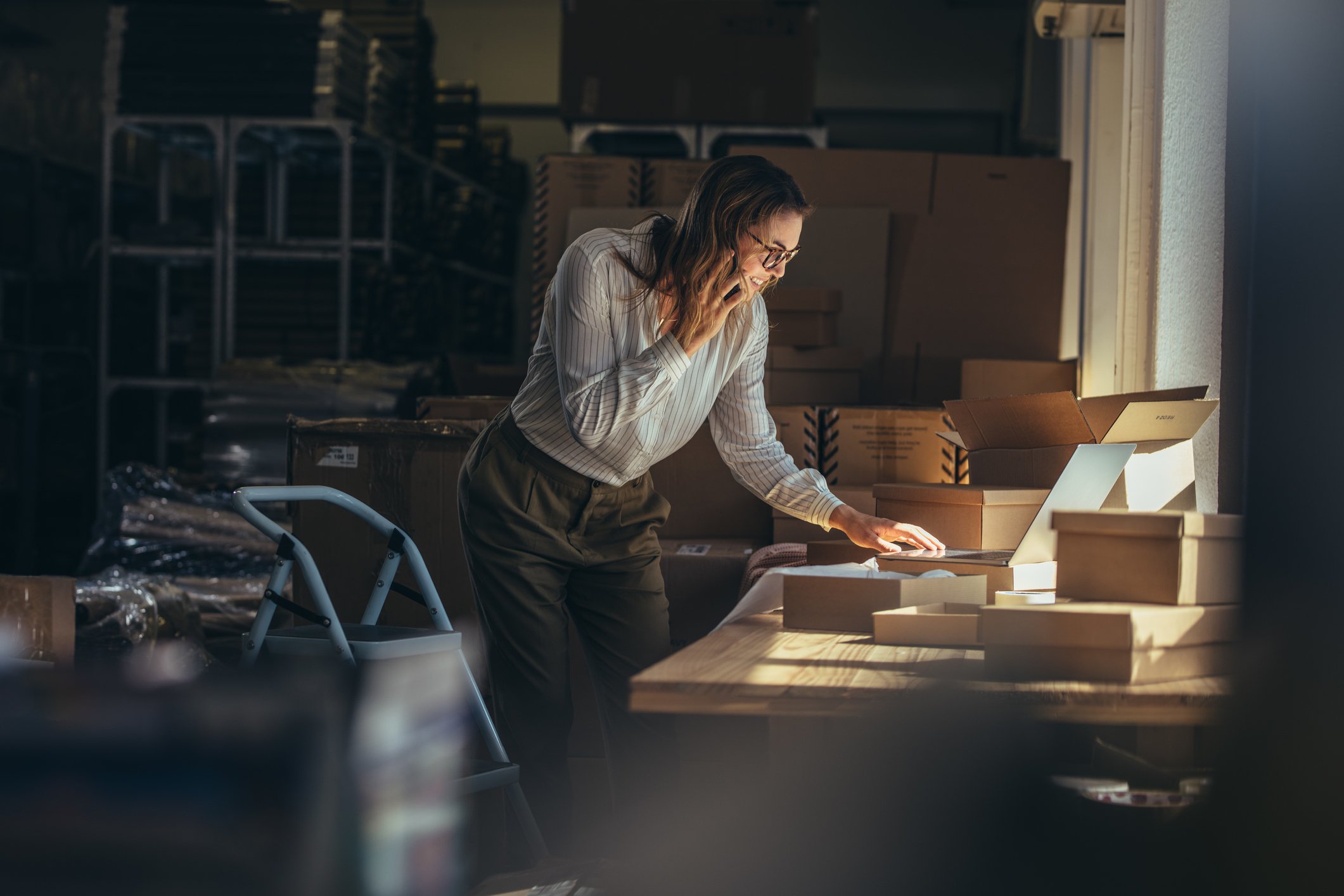 Entrepreneur in storage room with packages and checking inventory on computer