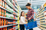 Mother and daughter browsing grocery aisle and placing items in blue shopping basket