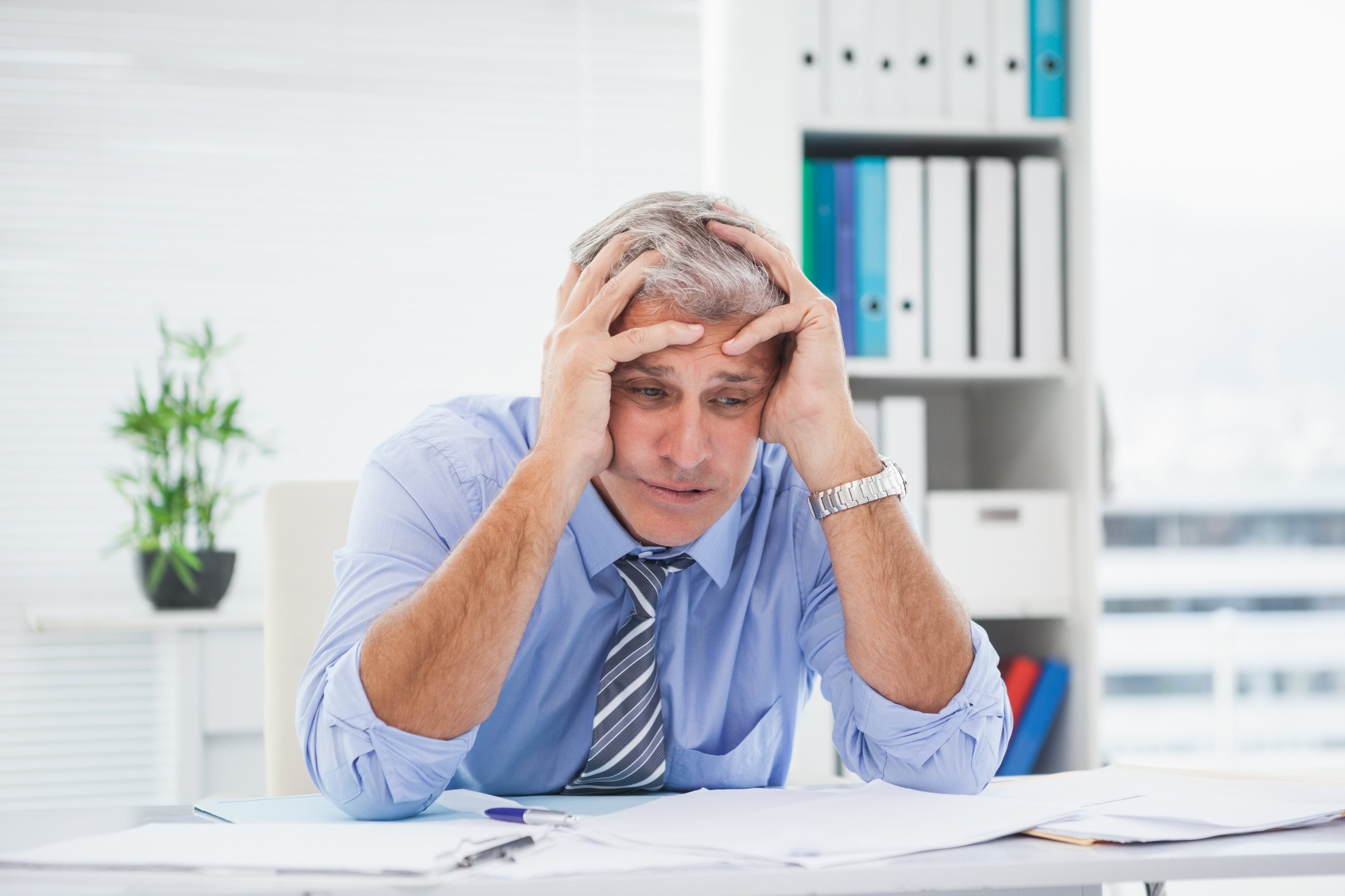 Stressed older adult male looking at papers and holding his head