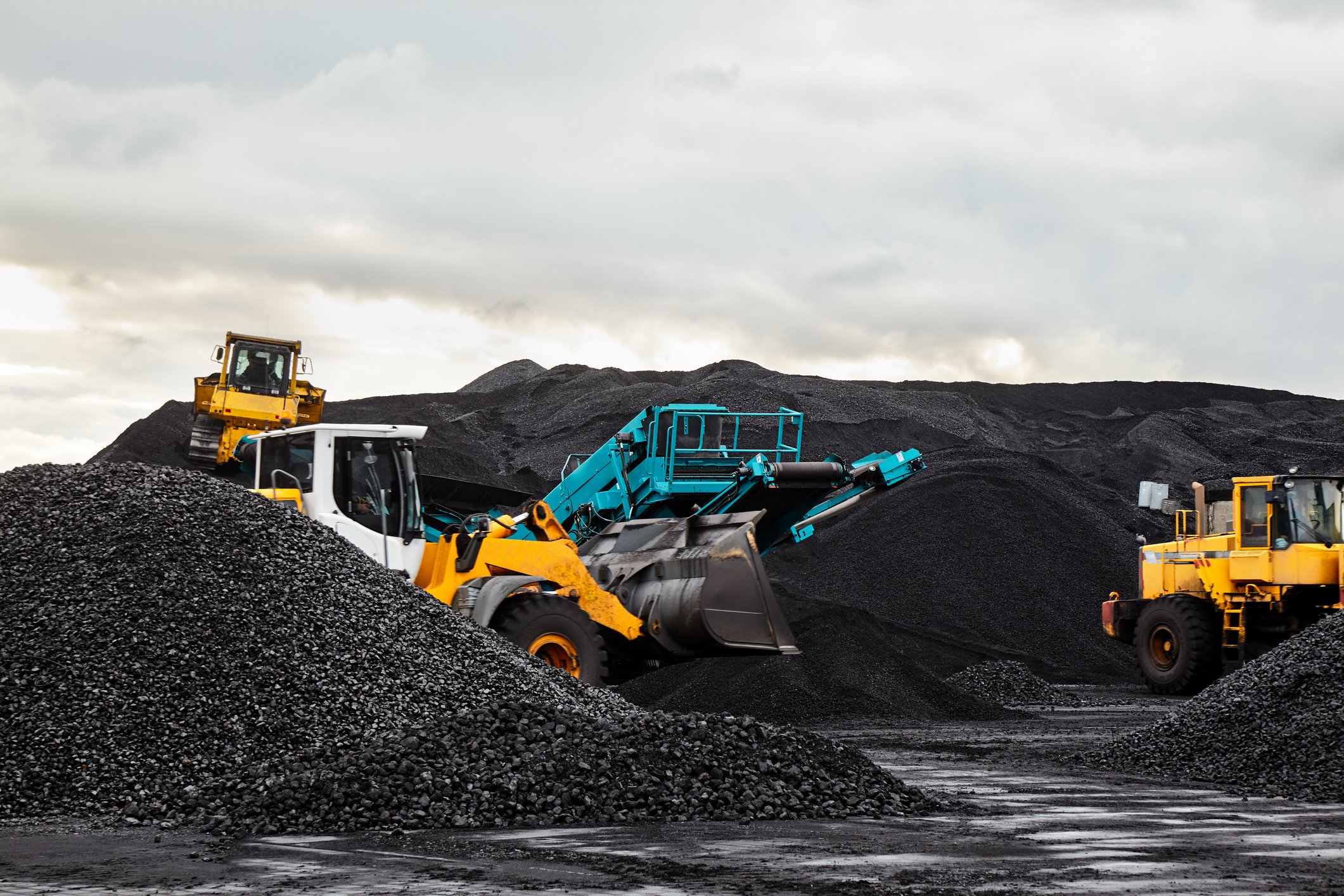 Two industrial sized trucks in a mining area with piles of raw material.jpg