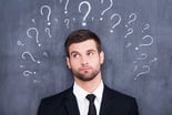Confused man question standing in front of chalkboard with question marks drawn around his head