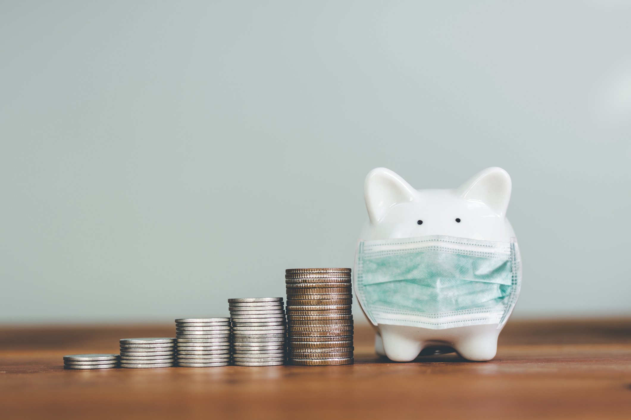 Piggy bank in mask next to rising stacks of coins