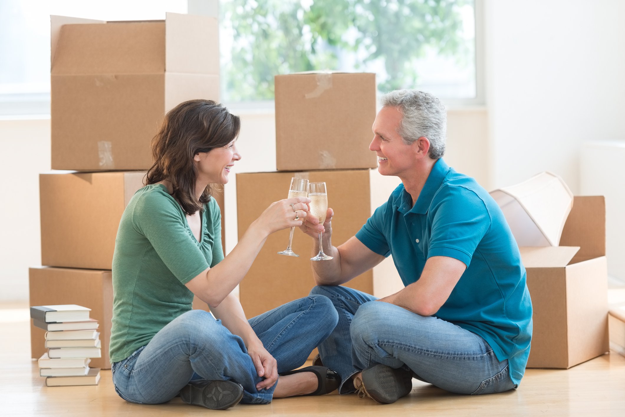 couple clinking champagne glasses surrounded by moving boxes.