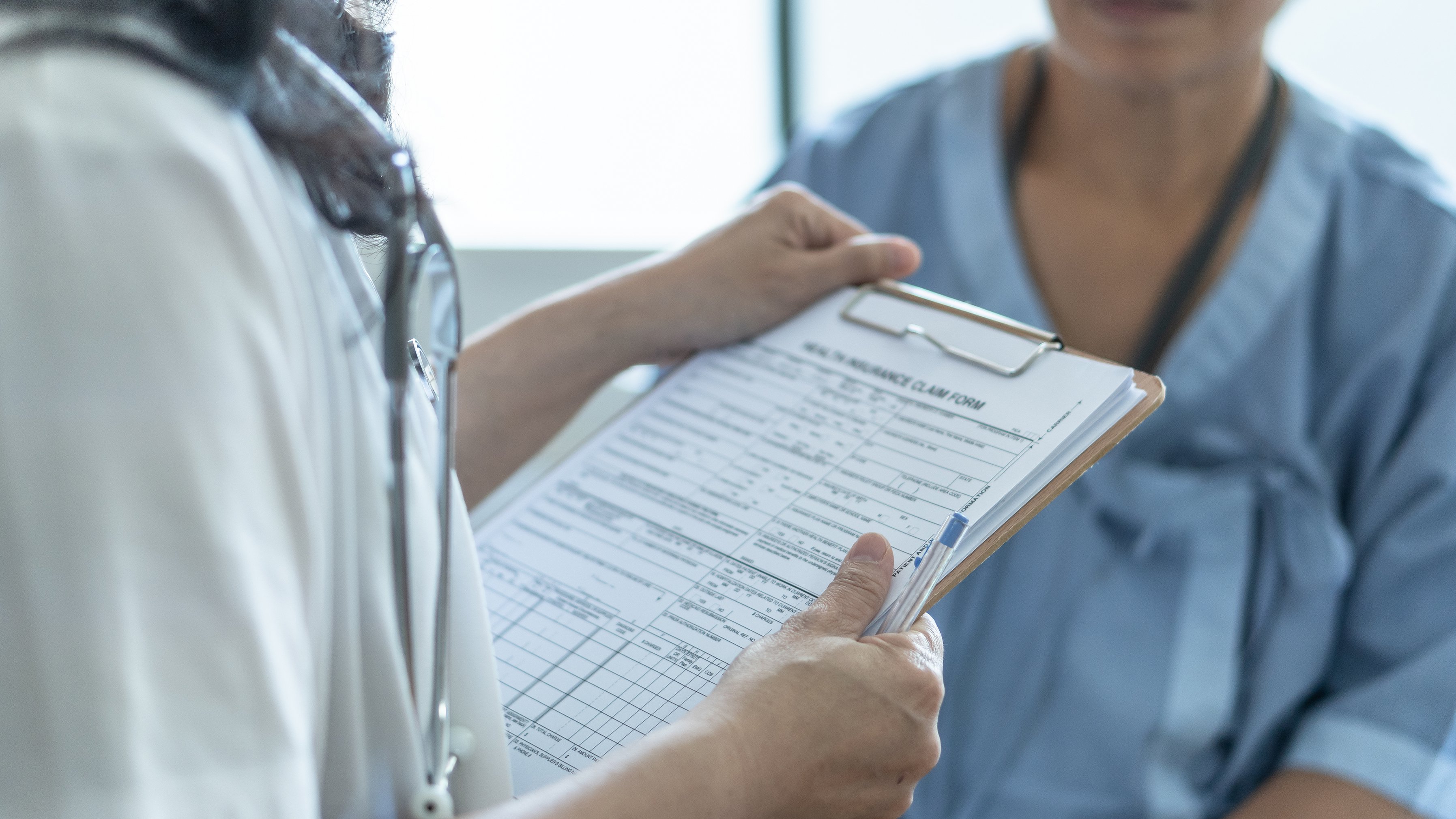 Doctor holding insurance claims form and talking with patient in hospital gown