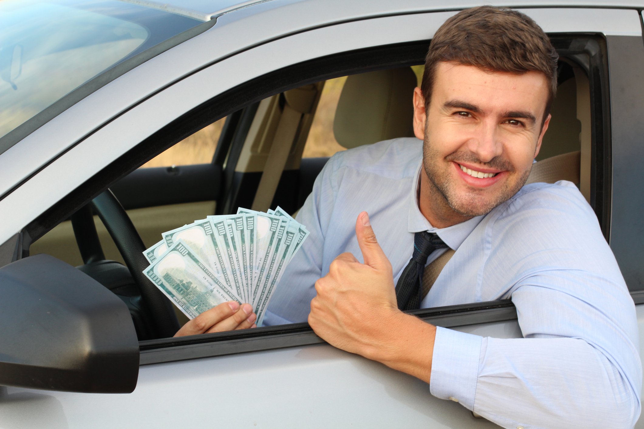 Driver leaning out of a car window holding hundred dollar bills