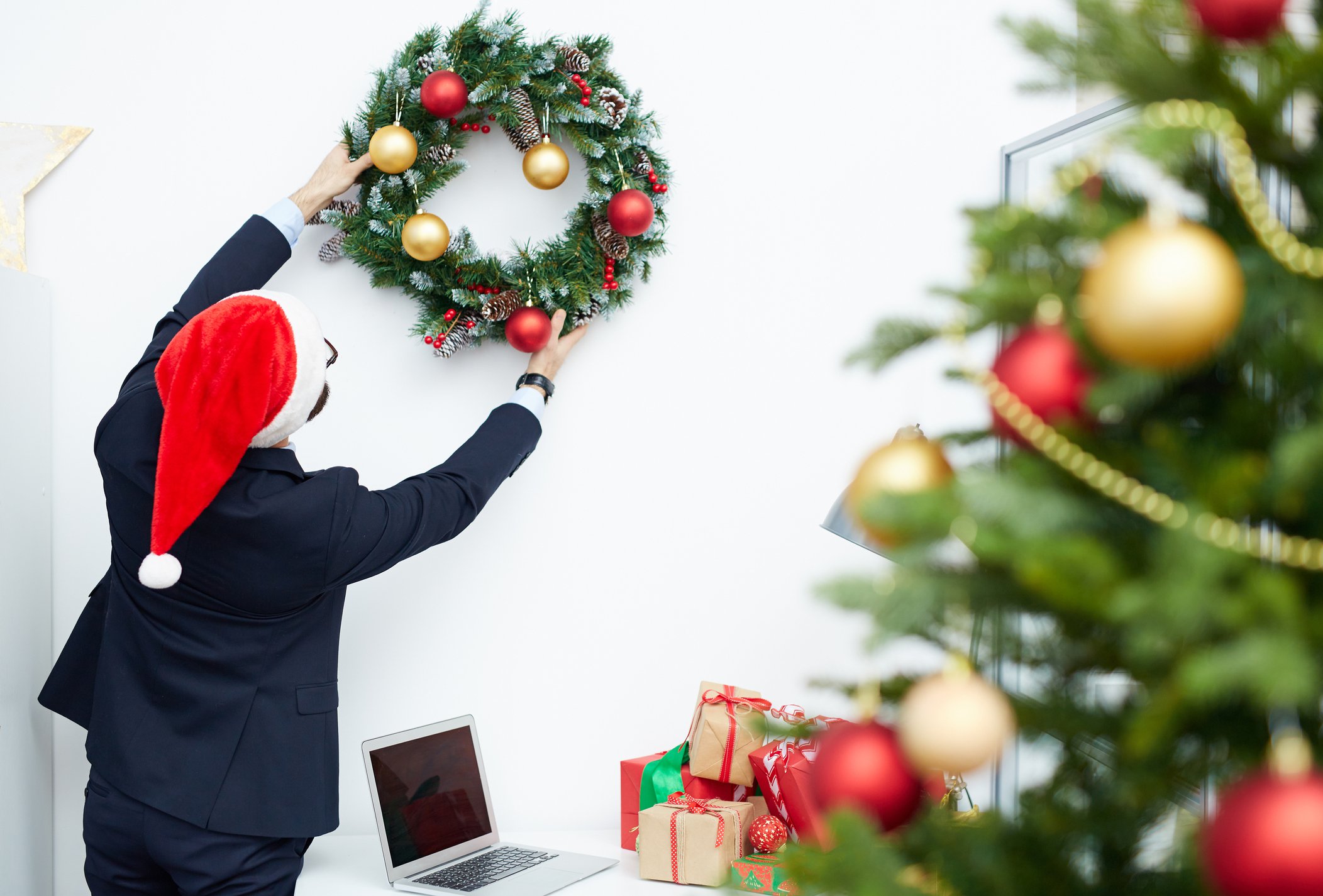 Man in a suit and Santa hat hanging a wreath