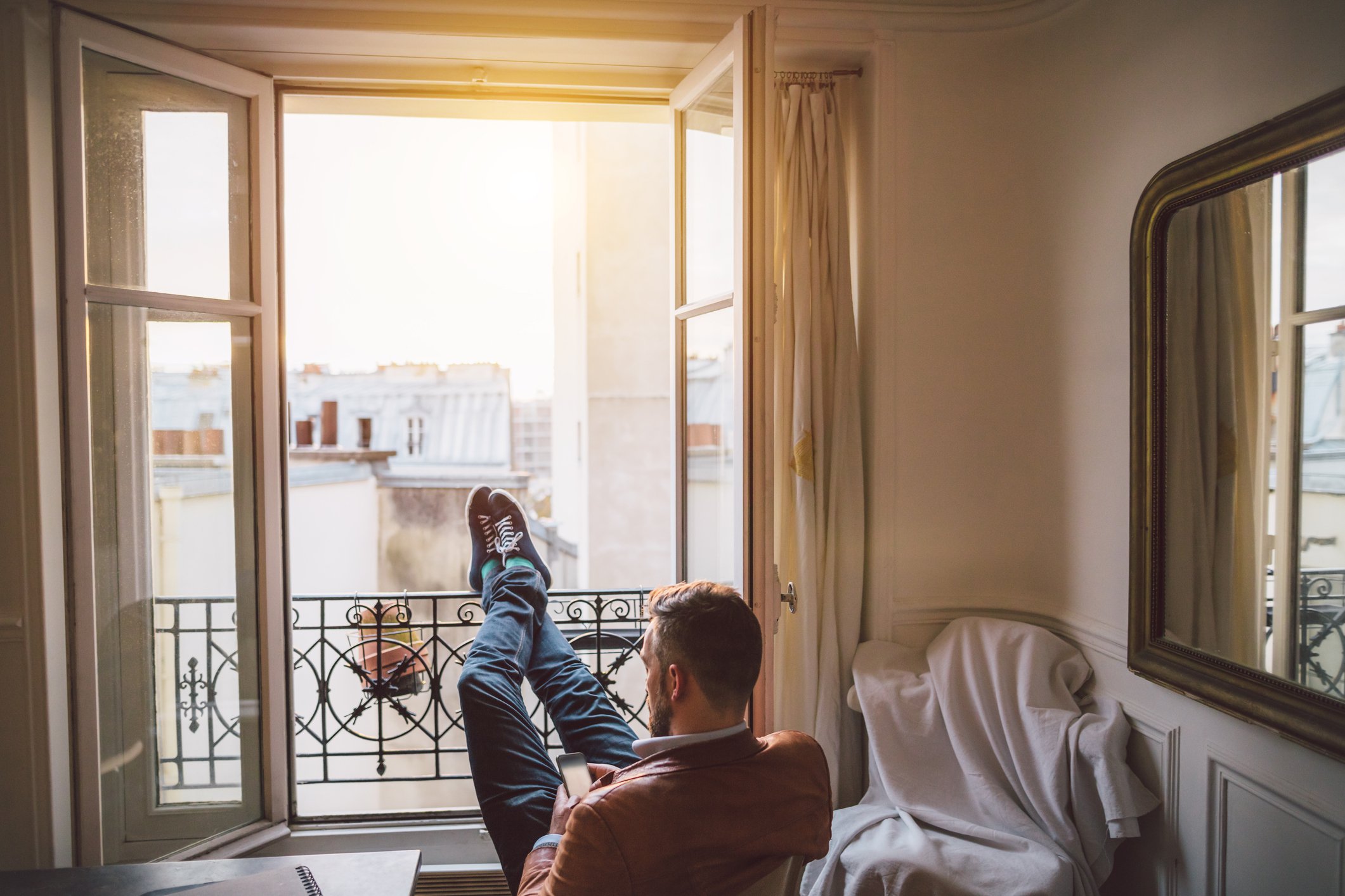 Man looking at phone and sitting with his feet up on open window railing