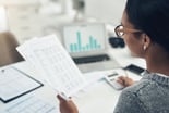 A woman looking at financial statements and typing numbers in a calculator.