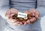 Person holds out hands holding pennies and a piece of paper that reads "retirement."