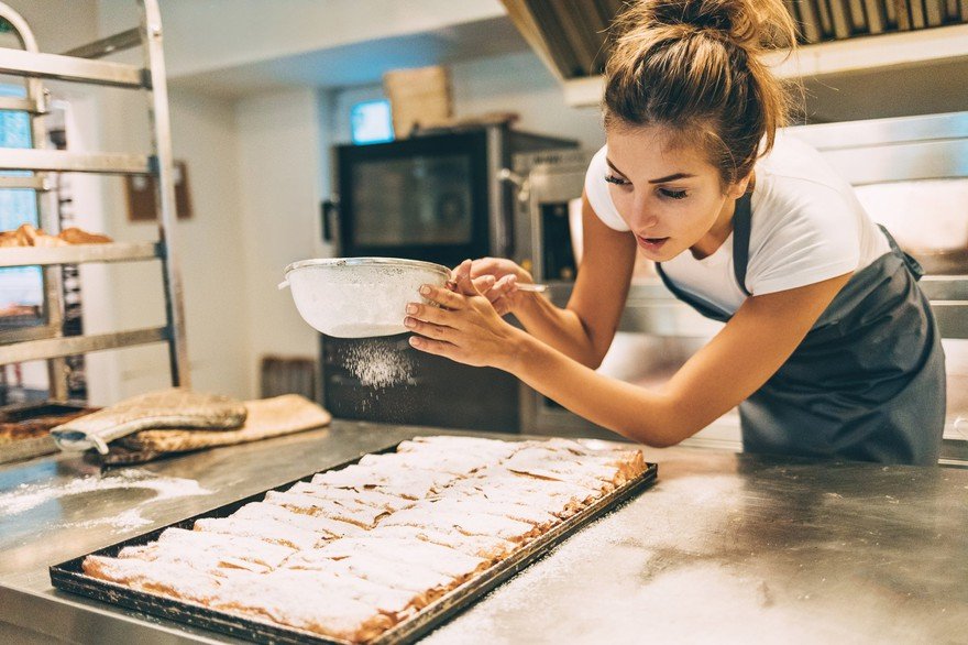 A person sprinkling sugar on some baked goods.