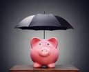 Piggy bank with an umbrella over its head.