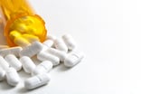 A prescription bottle overturned with pills pouring out.