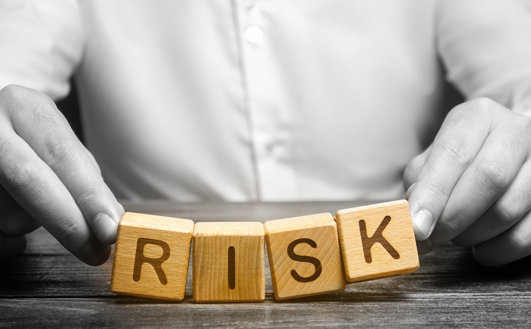 Person in white holding wooden blocks spelling Risk