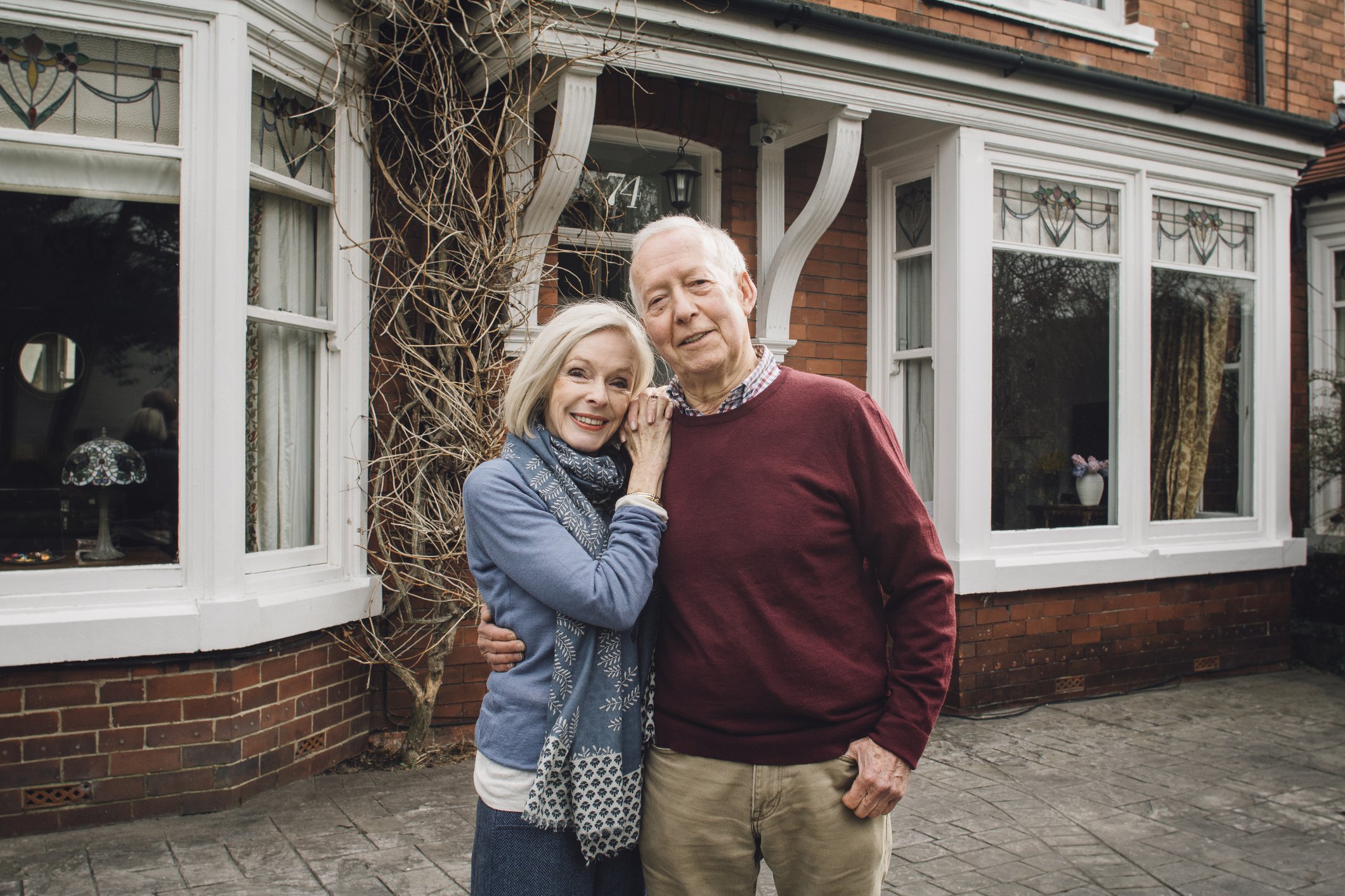 Senior man and woman smiling and holding each other in front of a house