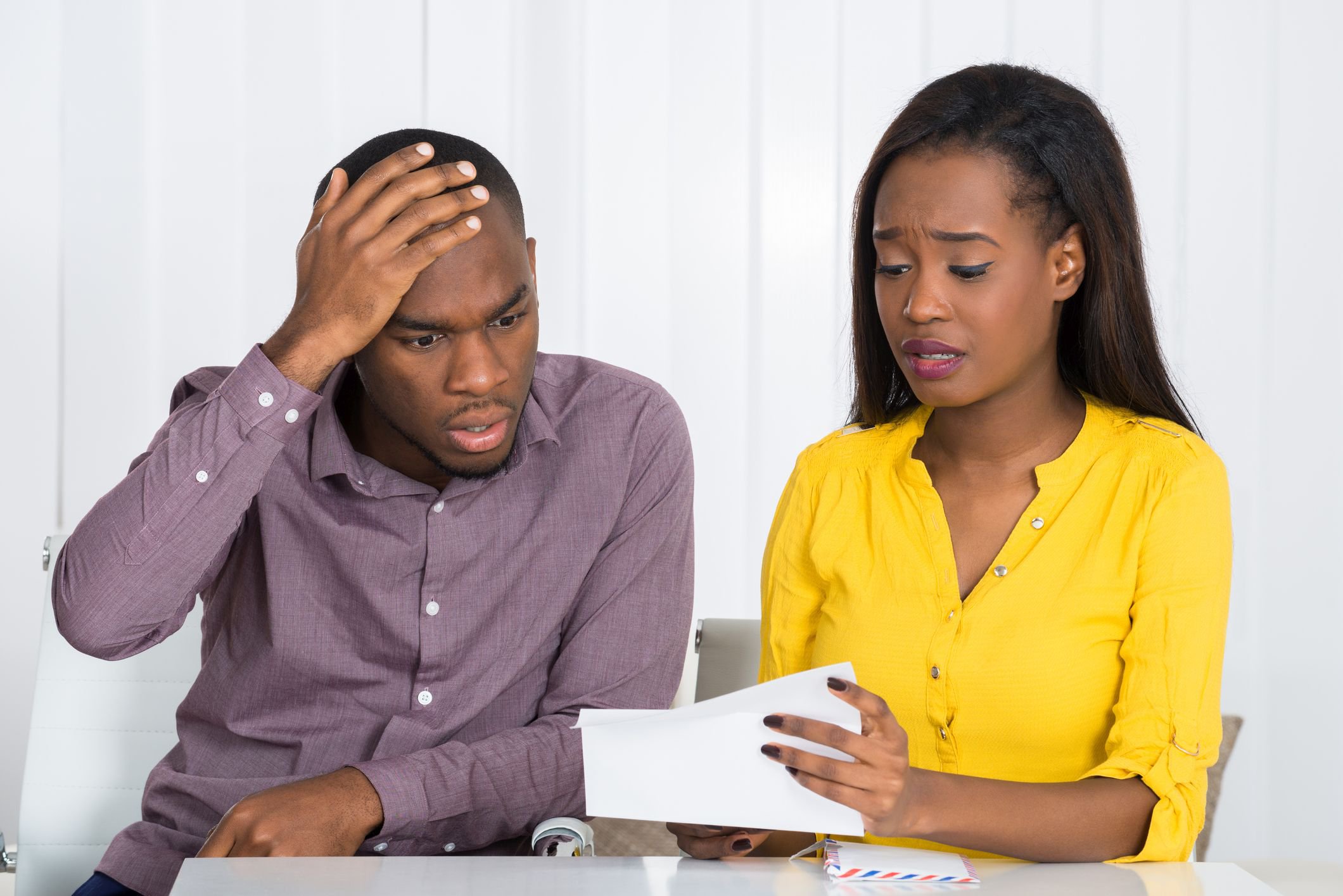 Young couple looks upset by mail they are reading.