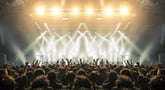 A crowd with hands in the air backlit by stage lights at a concert.