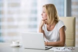 Woman at a laptop gazing out the window.