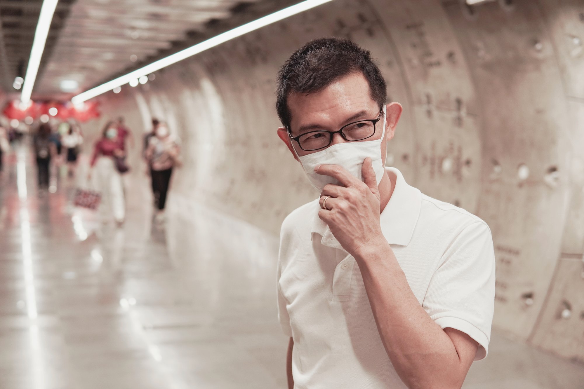 A man holding a mask to his face on a subway tunnel platform.