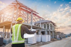 Worker looking at blueprints and standing outside a house being built.
