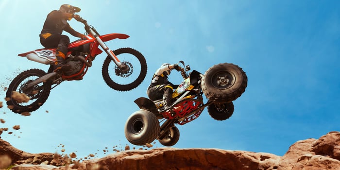 An ATV and motorcycle race across a desert landscape.