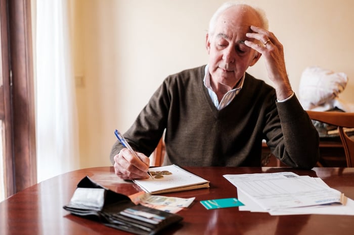 Older gentleman sitting at a table, concentrating as he makes notes.