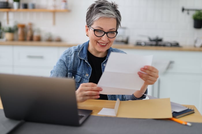 A person at a laptop holding a document.