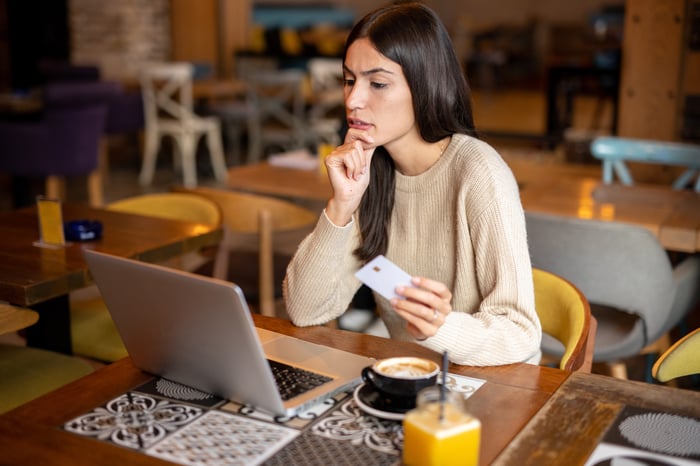 A person looks at a laptop and holds a credit card.