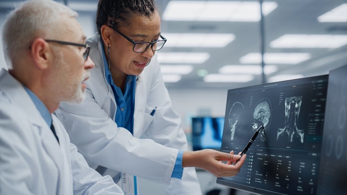 Two medical technicians in white lab coats looking at a brain scan on a computer display.